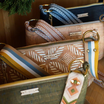 Close-up of a handbag with a strap featuring a decorative pattern, set against a wooden background.
